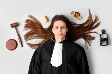 Young female judge with gavel and scales of justice lying on white background