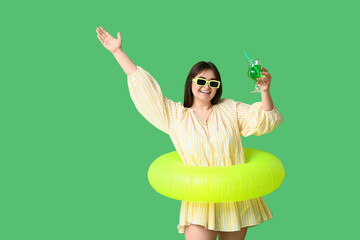 Beautiful young woman with inflatable ring and glass of cocktail on green background
