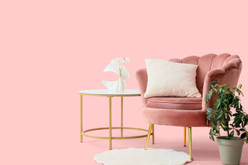 Beautiful armchair with houseplant, coffee table and rug on pink background
