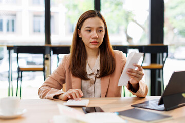 asian young woman hand checking list with bill for calculate accounting expense credit card payment on due deadline, trying to find money to pay debt on table. Business financial concept,