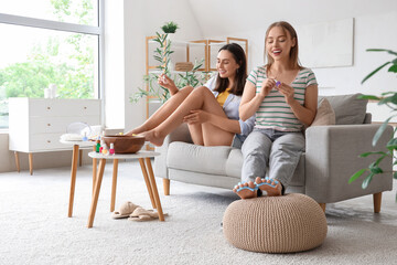 Young women with nail polishes making pedicure in living room