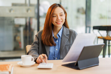 Fototapeta premium Asian female successful employee business freelance is holding document to reading business data and financial chart while working with laptop in the workplace office. 