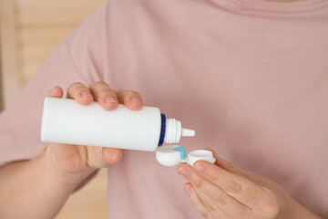 Young woman pouring solution in container with contact lenses at home, closeup
