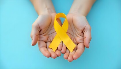 Hands grasping a yellow ribbon on a blue backdrop, highlighting support for Childhood Cancer Awareness Month