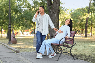 Young man calling ambulance for his wife having heart attack on bench in park