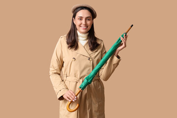 Happy young woman with umbrella on beige background