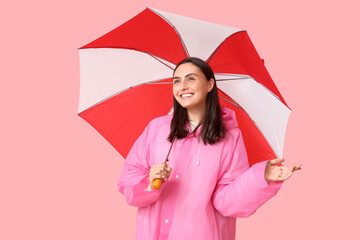 Young woman in raincoat and with umbrella on pink background