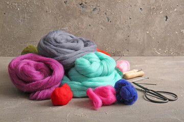 Heap of different wool for felting, needles and scissors on grunge background