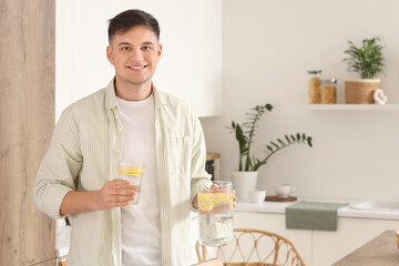 Young man with jug and glass of lemon infused water in kitchen