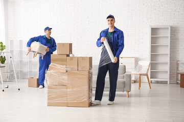 Male workers wrapping cardboard boxes with stretch film in room
