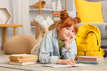 Teenage redhead girl with books lying on floor at home