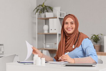 Female Muslim doctor working at table in clinic