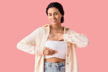 Young African-American woman checking her breast on pink background. Cancer awareness concept