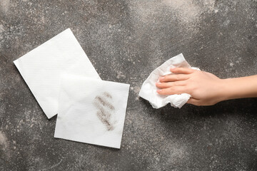 Woman wiping dust with paper napkins on grunge grey background