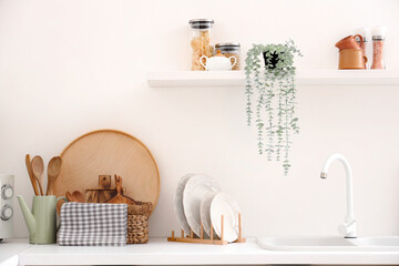 Counter and shelf with utensils on light wall in kitchen