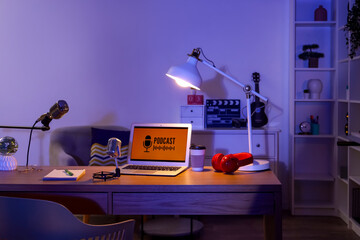 Podcaster's workplace with laptop, microphones and glowing lamp in dark studio