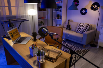 Podcaster's workplace with laptop and glowing lamps in dark studio