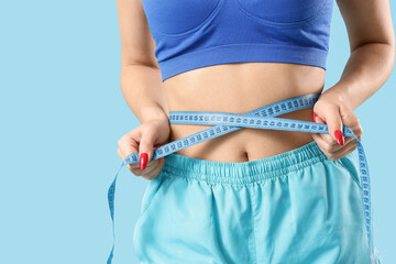 Sporty young woman measuring waist on blue background, closeup. Diet concept