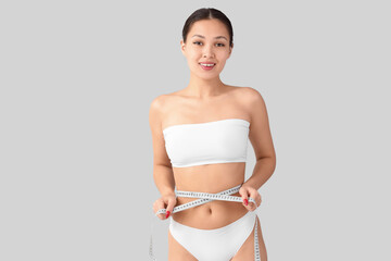 Young Asian woman in underwear measuring waist on light background. Diet concept