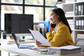 Asian businesswoman is talking on the phone with a customer and reading a monthly work schedule document.