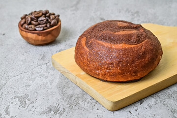 Close up view of coffee bun on wooden cutting board with roasted coffee beans in the little wooden bowl. grey or gray cement on background. bread home made. Mexican Coffee Bun.