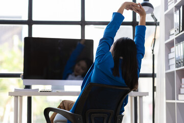 Businesswoman working on computer at office. She was stretching to relieve herself from sitting in an office chair for a long time.