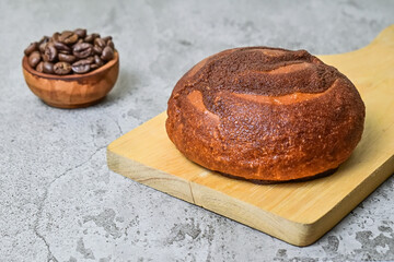 Close up view of coffee bun on wooden cutting board with roasted coffee beans in the little wooden bowl. grey or gray cement on background. bread home made. Mexican Coffee Bun.