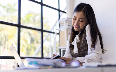 A serious female employee is busy with paperwork and talking on the phone with the boss.