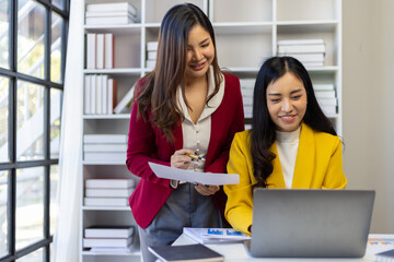 Asian businesswoman and colleague discussing new project on laptop in office.