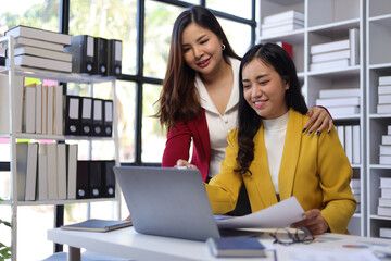 Asian businesswoman and colleague discussing new project on laptop in office.