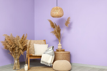 Wicker armchair, table and vases with pampas grass near violet wall in interior of room