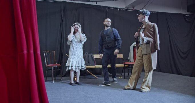 Young actors rehearse a play on stage. A man proposes to a woman while another actor observes.