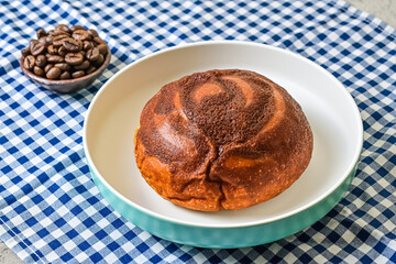 Close up view of coffee bun on plate with roasted coffee beans on little pottery or earthern plate isolated on napkin background. blue, white. bread home made. Mexican Coffee Bun.
