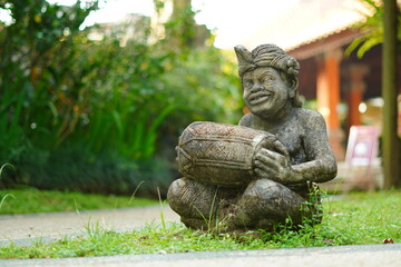 Balinese statue made of stone carved in the shape of a Balinese man sitting holding a traditional musical instrument.