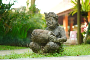 Balinese statue made of stone carved in the shape of a Balinese man sitting holding a traditional musical instrument.