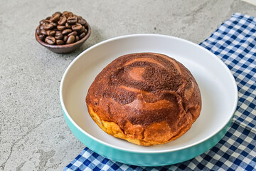 Close up view of coffee bun on plate with napkin. grey or gray cement as background. blue, white. bread home made. roasted coffee beans, little pottery or earthern.