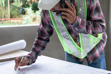 Indian construction project supervisor reading blueprint paperwork on table in building site using...