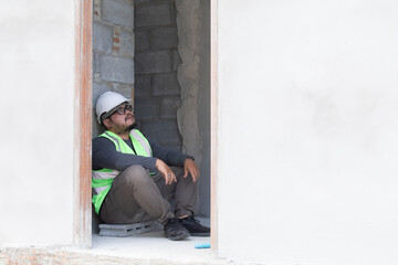 Young Asian engineering worker overweight employee foreman tired sitting on construction site,...