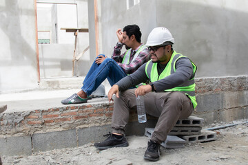 Two Asian builder workers wearing safety reflected vest and helmet tired thirsty hydrated drinking...