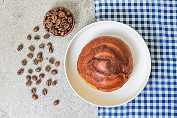 Top view of coffee bun on plate with napkin. grey or gray cement as background. High angle, above. blue, white. copy space, free, empty, negative. bread home made. coffee beans. scattered.
