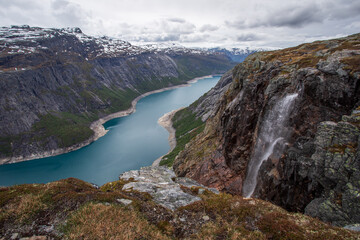 Cliff outlook of a waterfall and fjord leading to the far overcast distance