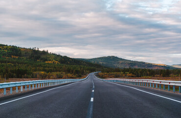 A long, open highway leads through a picturesque mountainous area.