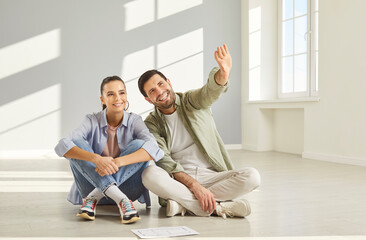 Young man pointing index finger discussing and planning repair with woman sitting on floor in empty new apartment. Happy couple thinking about interior decoration or design project. Moving concept.