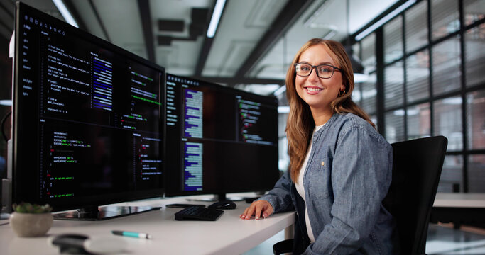 Smiling Female Developer Coding On Numerous Monitors