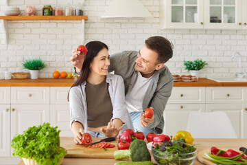 Happy healthy funny couple amuse cooking salad in modern kitchen, playing holding fresh vegetables, enjoying home activities, keeping healthy organic food diet together, vegetarians, vegan movement