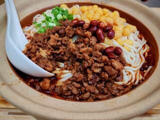 A flavorful bowl of ChongQing WanZha noodles topped with savory minced pork, chickpeas, roasted peanuts, and chopped spring onions, all served in a rich, spicy broth. Noodles with peas and meat sauce.