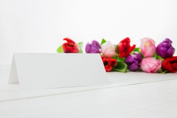 Flat design is showing blank white folded tent card on white tabletop with blurred colorful tulips