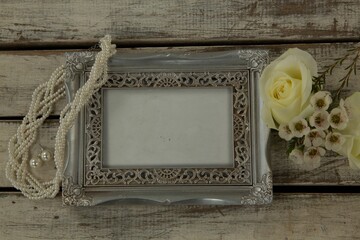 Photo frame, necklace and flowers on wooden table