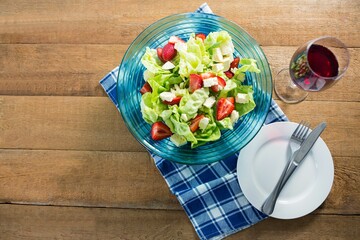 Fresh salad in bowl with red wine on wooden table