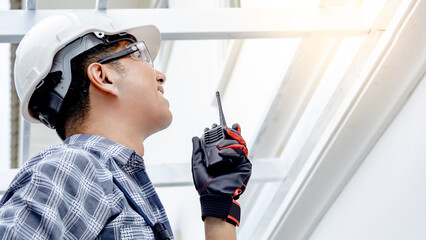 Asian male foreman talking on walkie talkie while looking at roof structure. Civil engineer man...